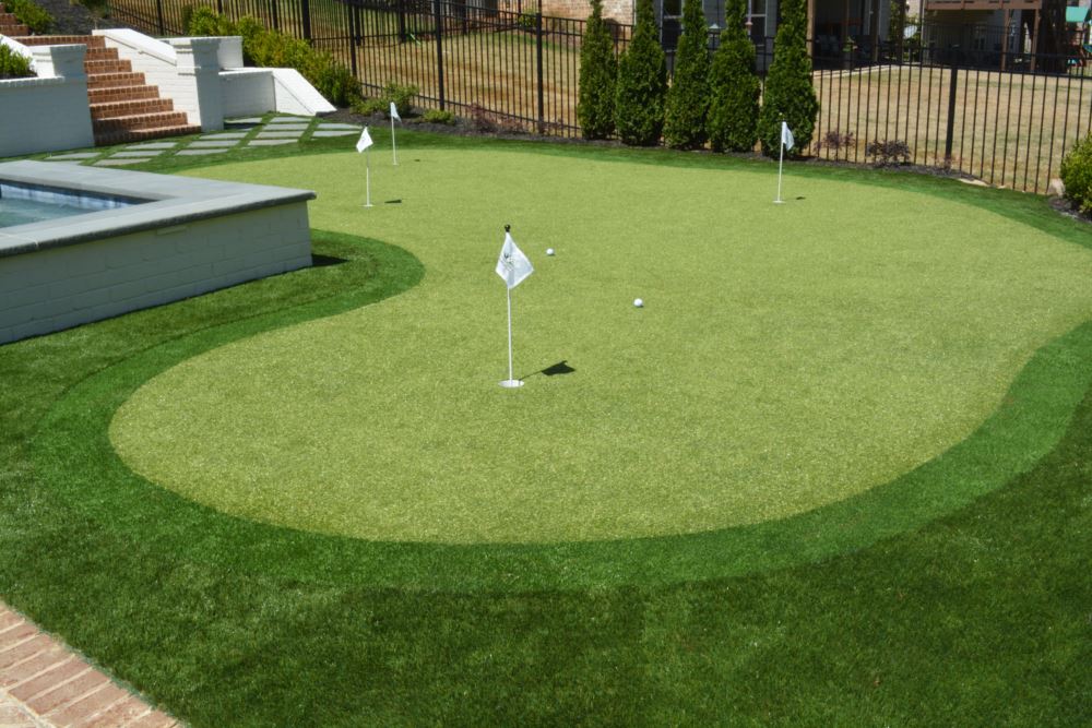 Backyard putting green built with artificial grass with hole flags and steps in the background.