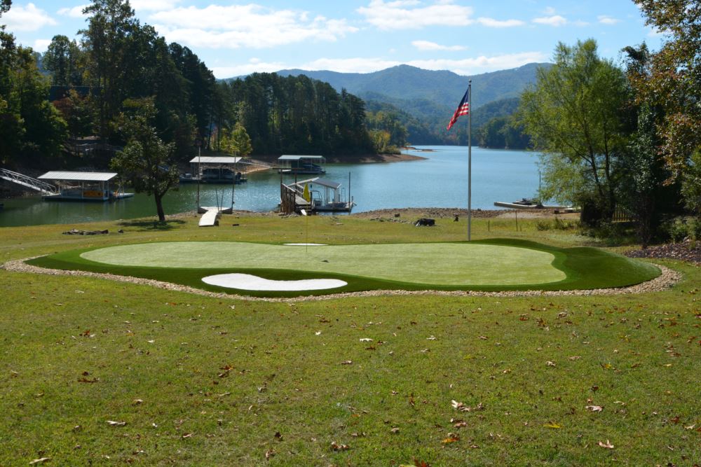 Artificial turf putting green installed in front of a lake with mountains and the American flag in the background.