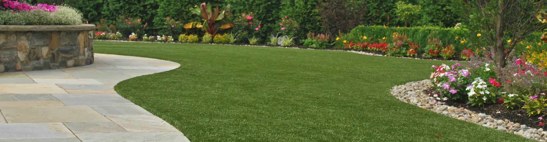 Southwest Greens lawn turf grass edging a curved stone patio surrounded by vibrant flowering garden beds and manicured hedgerows.